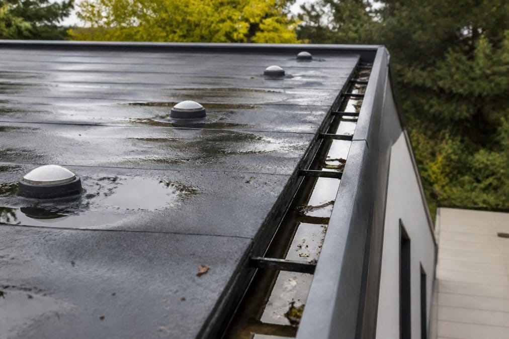 Close-up of flat roof surface with visible drainage guttering system, water management channels, and maintenance access points in natural daylight