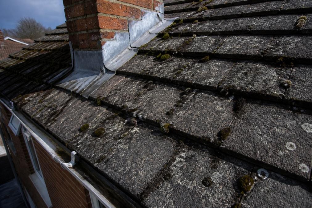 Close-up view of deteriorated roof tiles with visible moss growth, cracked flashing, and water staining on residential roof surface