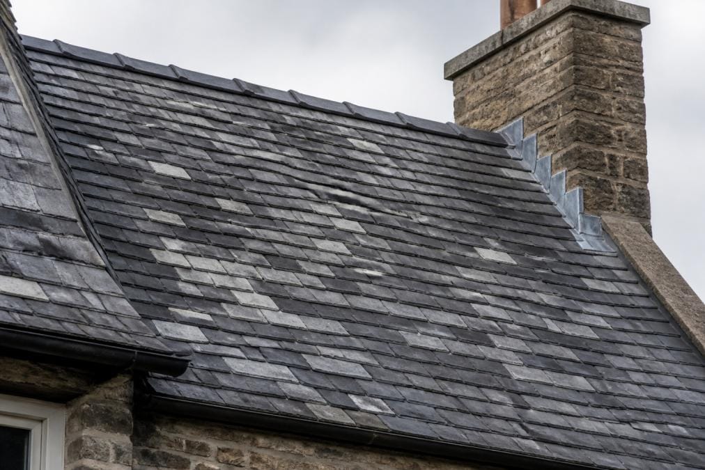 Close-up of a slate roof on a period property showing natural stone tiles with varied grey and dark tones, demonstrating the texture and weathered appearance of traditional slate roofing