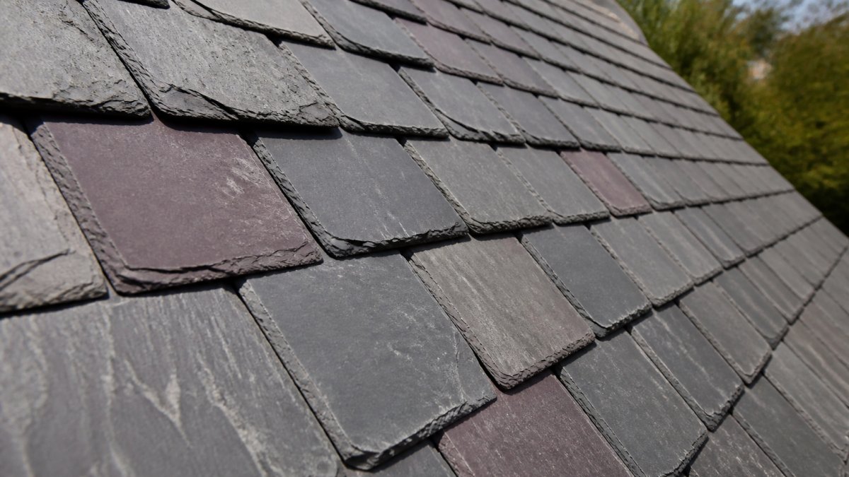 Close-up of natural slate roof tiles with textured grey and purple surfaces, showing the distinctive layered pattern and natural grain of slate material in afternoon sunlight
